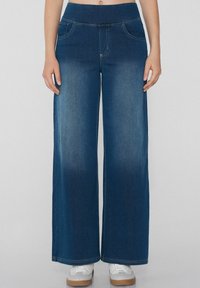 Jeans de denim de pierna ancha en azul oscuro, con una cintura suave, dos bolsillos frontales y un leve desgaste a lo largo de las piernas.