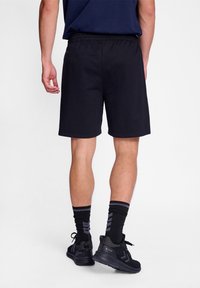 Black cotton shorts with an elastic waistband, reaching mid-thigh, paired with black and gray socks and athletic shoes.