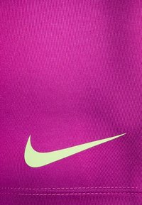 Fuksia Nike urheilu kangas, jossa on sileä pinta, ja joka esittelee näyttävän vaaleanvihreän swoosh-logon vasemmassa alakulmassa.