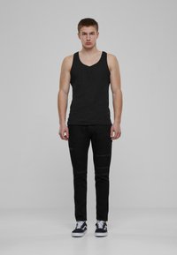 Débardeur en coton noir avec un design à col en V, associé à un jean en denim noir déchiré et des baskets noires avec des semelles blanches.