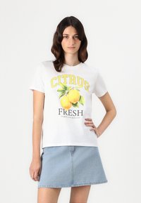 Balta medvilninė marškinėliai su geltonu užrašu „CITRUS“ ir grafika, kurioje pavaizduoti citrinos su žalios lapeliais. Suderinti su mėlynu džinsiniu sijonu.