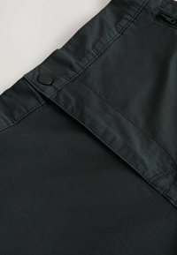 Schwarzer Stoff mit glatter Textur, Knopfverschluss und detaillierten Nähten an den Kanten. Sauberes Design ohne sichtbare Muster oder Akzente.