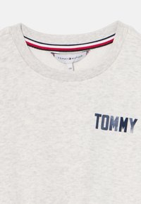 Šviesiai pilka džemperis su apvaliu kaklu, geležimi apvadu ir tamsiai mėlynu "TOMMY" logotipu priekyje. Minkšta tekstūra su subtiliu heather raštu.