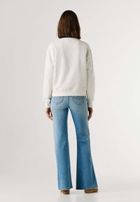 Λευκό φούτερ με ραβδωτά μανσέτες, σε συνδυασμό με ανοιχτόχρωμο τζιν παντελόνι με φαρδιά καμπάνα. Λείο ύφασμα, απλός σχεδιασμός και χωρίς ορατά σχέδια ή λεπτομέρειες.