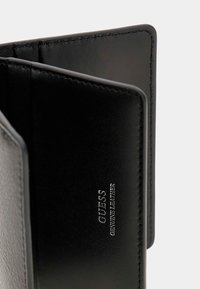 Portafoglio in pelle nera con una texture liscia, dotato di più slot per carte e dettagli in rilievo "GUESS GENUINE LEATHER".