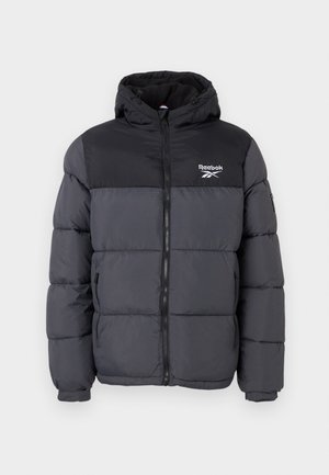 Jachetă puffer neagră și gri cu glugă, având un fermoar frontal, manșete elastice și un logo Reebok pe piept. Textură moale, matlasată.