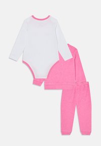 L'ensemble comprend un bodysuit à manches longues blanc avec un liseré rose, ainsi qu'un haut et un pantalon roses avec un motif texturé.
