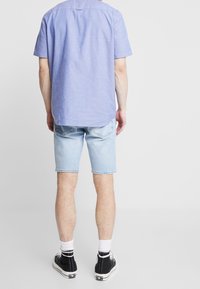 Světle modrá košile s krátkým rukávem vyrobená z texturované látky, v kombinaci se světle modrými džínsovými šortkami. Černé tenisky s bílými akcenty.