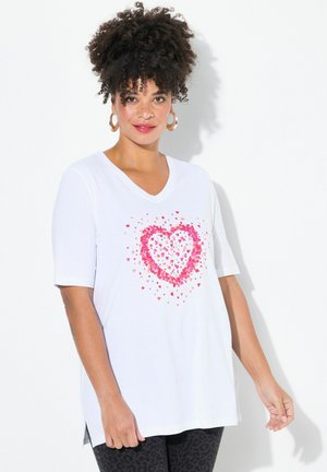 T-shirt blanc à col en V avec des manches courtes, présentant un design de cœur rose composé de divers petits cœurs. Tissu doux avec des fentes sur les côtés à l'ourlet.