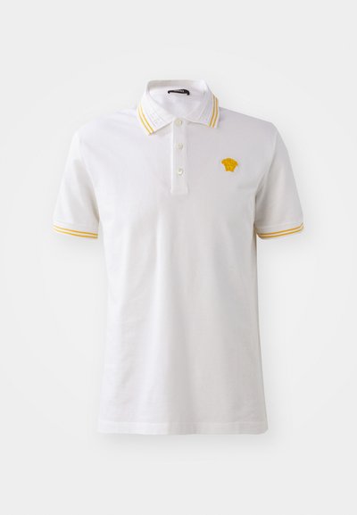 Biela polo košeľa z bavlny s žltými pruhmi na golieri a rukávoch, s vyšitým logom na hrudi.