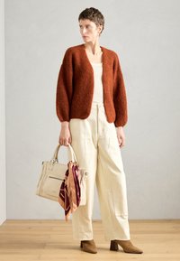 Rustfarvet sweater med fluffy tekstur, cremede top, beige vid bukser, brune hælede støvler og en lys taske prydet med et mønstret tørklæde.