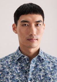 Camicia di cotone con motivo paisley blu e bianco, con colletto a punta e chiusura con bottoni. Tessuto liscio e design aderente.