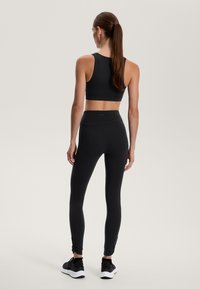 Fekete sportmelltartó és leggings, rugalmas anyagból készült. A leggings boka része kivágott, fekete sportcipővel párosítva. Egyszerű dizájn.