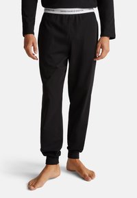 Zwarte katoenen loungebroek met elastische tailleband, voorzien van een wit merkembleem, taps toelopende boorden en een relaxte pasvorm.