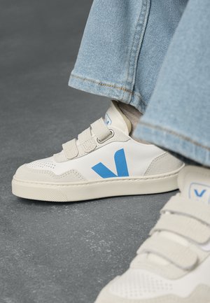 Hvite sneakers med blå detaljer, med en glatt læroverdel, perforert tå og borrelåsremmer. Teksturert gummisåle.