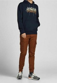 Felpa con cappuccio navy con grafica "Jack & Jones" multicolore, pantaloni cargo marroni con cinturini elasticizzati e scarpe da corsa grigie con dettagli arancioni.