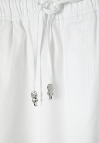 Białe spodnie z troczkami, zakończone srebrnymi agletami w kształcie zawieszek, zwisającymi z zawiązanych sznurków w pasie.