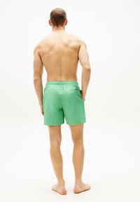 Bañador verde con cintura elástica, acabado con un bolsillo trasero que presenta un pequeño acento de color. Textura ligera y suave.