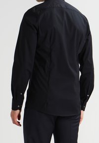 Zwart shirt met lange mouwen van gladde stof met manchetten met knopen en een puntige kraag. Heeft een getailleerd ontwerp en een afgeronde zoom.