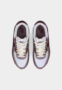 Ζευγάρι λευκά και μαρόν αθλητικά παπούτσια Nike με εκρού κορδόνια, φωτογραφημένα από πάνω σε απλό λευκό φόντο.