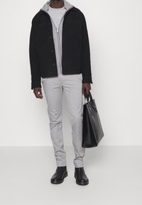 Chaqueta negra de botón con sudadera gris, camiseta gris, pantalones gris claro, botas negras hasta el tobillo y bolso tote negro.
