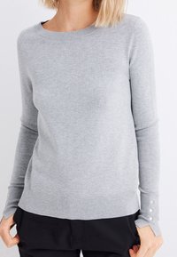 Grauer Strickpullover mit langen Ärmeln, Rundhalsausschnitt, geripptem Saum und Knopfakzenten an den Manschetten. Weiche Textur, schlichtes Design.