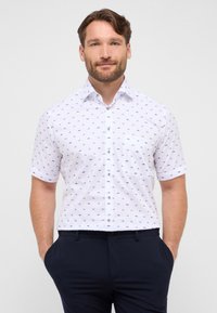 Korte mouwen witte blouse met kleine blauwe patronen, knoopsluiting aan de voorkant, kraag en een enkele borstzak, gecombineerd met donkere broek.