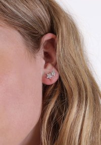 Silberne blumenförmige Ohrringe sind mit mehreren kleinen klaren Kristallen besetzt, die ein zartes, strukturiertes Muster bilden. Sie sind auf einem Stecker-Hintergrund befestigt.
