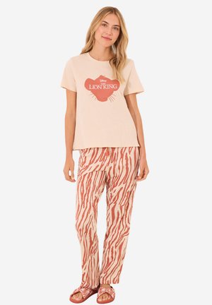Beige katoenen T-shirt met rode Lion King graphic; gecombineerd met lichtgewicht, roodgestreepte wijde broek; gedragen met platte sandalen.