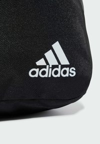 Borsa in tessuto nero con superficie testurizzata, che presenta un logo Adidas bianco e tre strisce parallele nell'angolo inferiore.