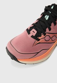 Różowy but do biegania z teksturowaną siateczkową cholewką, czarnymi sznurowadłami, pomarańczową podeszwą środkową i subtelnym wzorem na boku.
