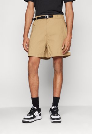 Lysbrune knælange shorts med en struktureret finish, der har et sort bælte og sidelomme. Særskilt med sort og hvidt sneakers.