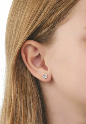 Close-up of a person’s ear with straight blonde hair, wearing small silver butterfly-shaped stud earrings with embedded clear stones.