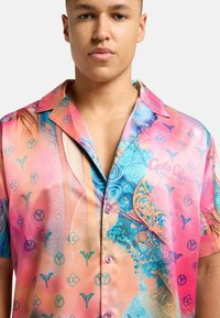 Fargerik kortermet skjorte med et livlig rosa og blått mønster med sirkulære og blomstermotiver. Laget av lett, skinnt stoff.