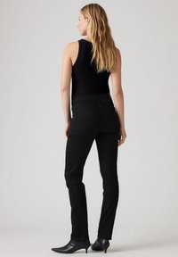 Jeans ajustados negros con cintura de media altura, bolsillos delanteros y traseros, y costuras sutiles. Combinados con botas de tacón negro hasta el tobillo.