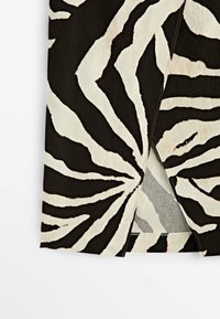 Tissu à imprimé animal noir et blanc avec des coutures visibles, plié pour révéler une petite ouverture triangulaire.