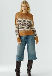 Gebreide trui met een fair isle patroon in warm bruin, crème en blauw. Geribbelde manchetten en zoom, gecombineerd met lichtblauwe denim shorts met wijde pijpen en bruine laarzen.