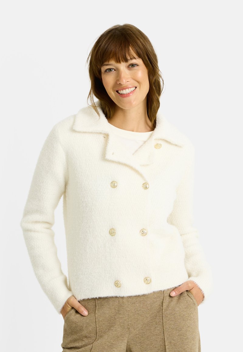 Chaqueta suéter blanca de doble botonadura hecha de un material suave y texturizado, con cuello y botones dorados. Diseñada con mangas entalladas.