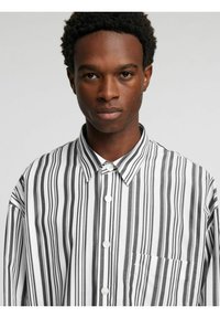 Svart- og hvitstripet skjorte med knapp ned-krage, utstyrt med en enkel brystlomme og glatt stofftekstur.