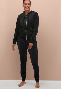 Zwarte velourse hoodie met rits aan de voorkant en twee zakken, gecombineerd met bijpassende joggingbroek, beide met een zachte, gladde textuur.