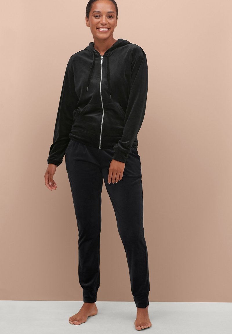Zwarte velourse hoodie met rits aan de voorkant en twee zakken, gecombineerd met bijpassende joggingbroek, beide met een zachte, gladde textuur.