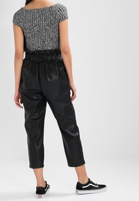 Pantalones de imitación de cuero negros de cintura alta con un cinturón en la cintura, combinados con una blusa de punto gris texturizada y zapatillas negras, vistos desde la parte de atrás.