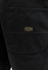 Poche de pantalon en tissu noir avec une petite étiquette rectangulaire de la marque Jack & Jones cousue au centre.