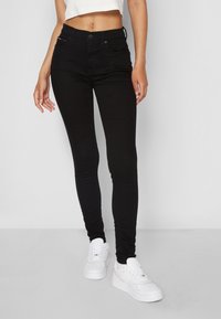 Jeans neri skinny con vita media, caratterizzati da tasche frontali e un design minimale. Abbinati a sneaker bianche per un contrasto.