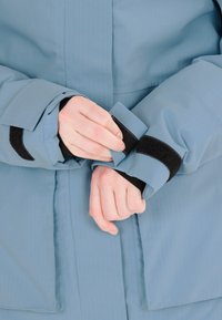 Blå vattentät jacka med en slät yta, som har kardborreband vid ärmsluten och en minimalistisk design.