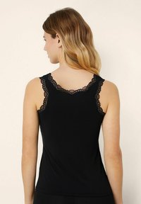 Černý tílko s jemnou krajkovou výšivkou kolem výstřihu a armhole, vyrobené z měkké jersey tkaniny, přiléhavý střih.