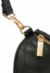 Czarna pikowana skórzana torba o zaokrąglonym kształcie, ze złotymi akcentami, wyraźnym uchwytem suwaka i odpinanym paskiem.