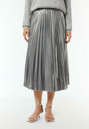 Person wearing a gray cable knit sweater, metallic silver pleated midi skirt, and silver open-toe high heel sandals on white background.