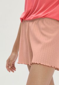 Helle rosa gerippte Shorts mit einem gewellten Saum. Hergestellt aus weichem Stoff mit vertikalen Streifen und kleinen dekorativen Löchern.
