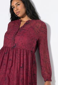 Bordeaux jurk met lange mouwen en knopenoverlapping, met een zwart sterrenpatroon en een geplooide taille voor een vloeiende silhoeet.